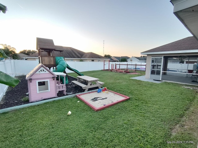 yard at dusk featuring a fenced backyard, a playground, and a sunroom
