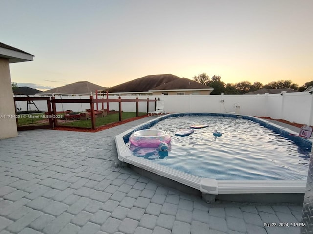 pool at dusk featuring a patio area, a fenced backyard, and a fenced in pool