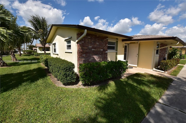 view of side of home with brick siding, a lawn, and stucco siding