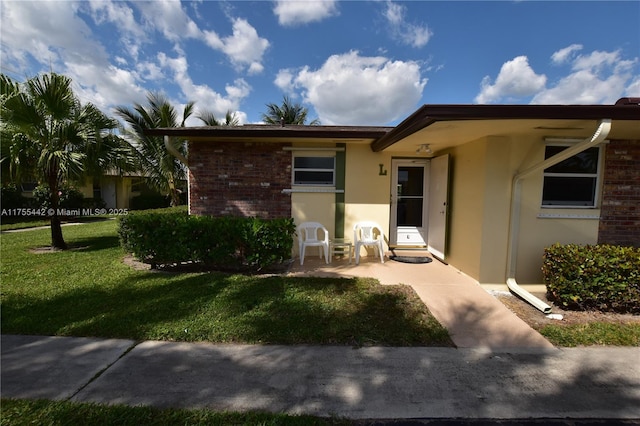 doorway to property featuring brick siding, a yard, and stucco siding