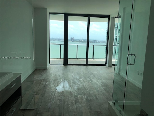 spare room with a wall of windows, a water view, baseboards, and wood finished floors