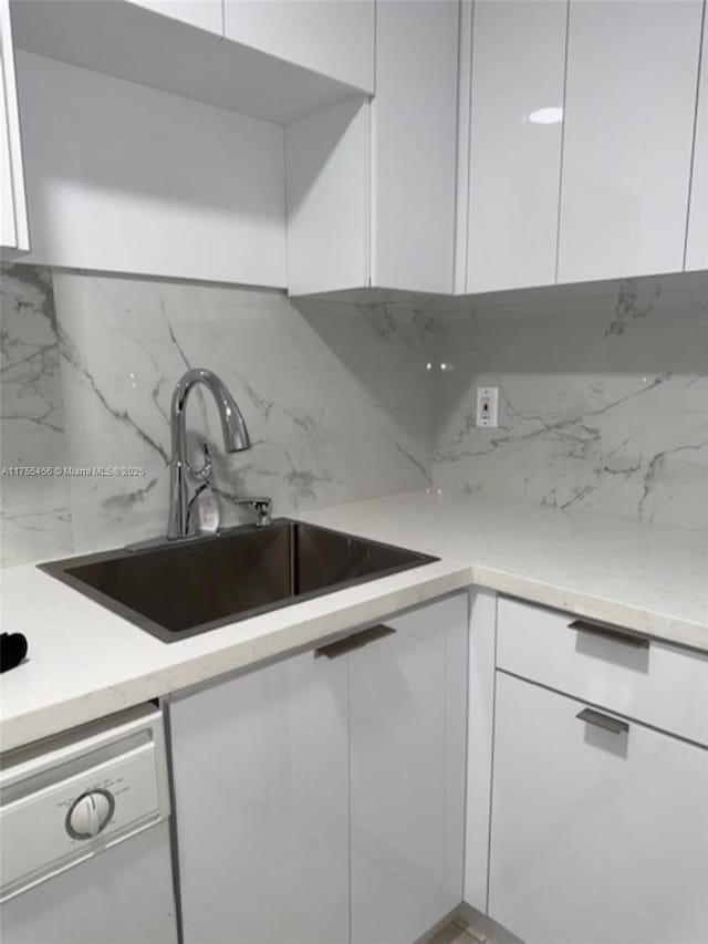 kitchen with white dishwasher, a sink, and white cabinetry