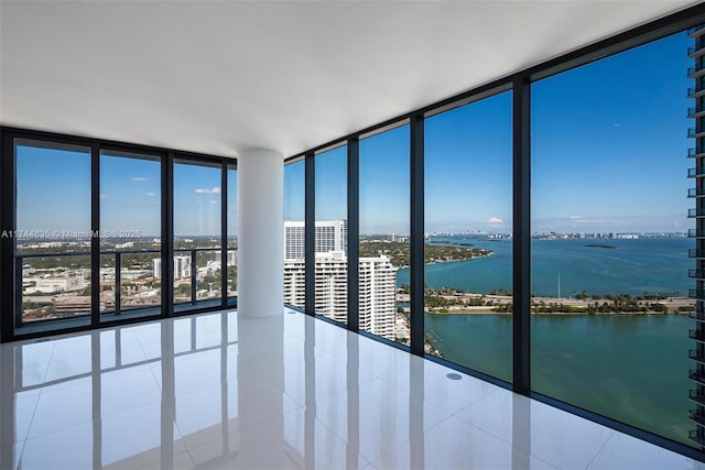 tiled spare room with a view of city, floor to ceiling windows, and a water view