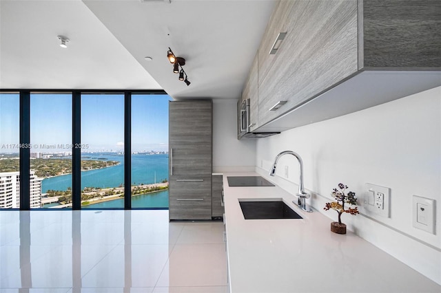 kitchen featuring light tile patterned floors, a water view, a wall of windows, light countertops, and a sink