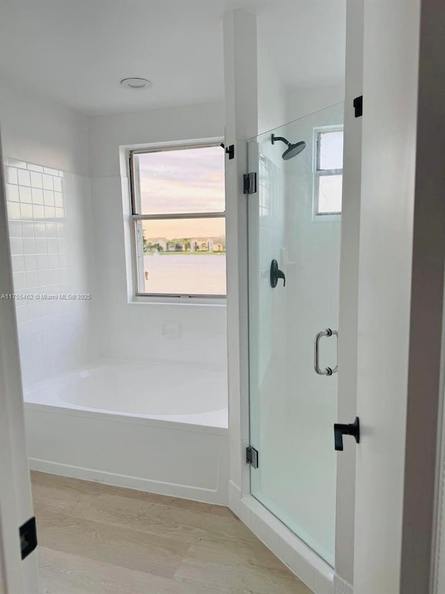 full bathroom with a healthy amount of sunlight, a garden tub, a shower stall, and wood finished floors