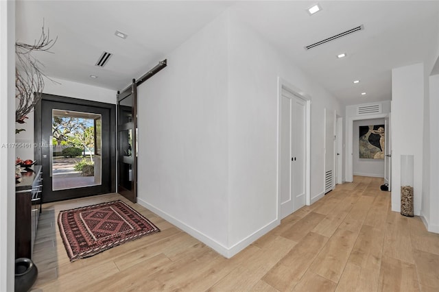 hallway featuring light wood-type flooring, a barn door, visible vents, and baseboards