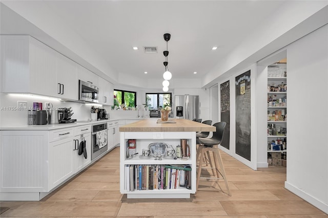 kitchen with light wood finished floors, stainless steel appliances, visible vents, white cabinets, and a kitchen island