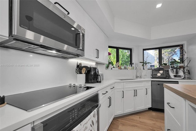 kitchen with light wood-style flooring, stainless steel appliances, a sink, white cabinetry, and a raised ceiling