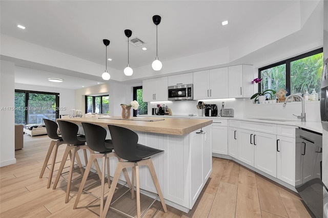 kitchen featuring visible vents, stainless steel microwave, light countertops, light wood-type flooring, and a sink