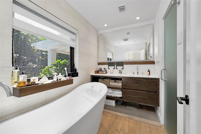 bathroom featuring double vanity, visible vents, wood finished floors, a freestanding bath, and a sink