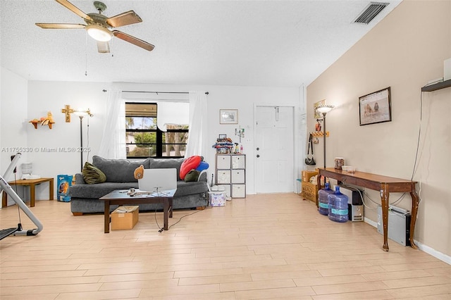 living area featuring a ceiling fan, visible vents, light wood-style flooring, and a textured ceiling