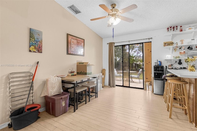 home office with vaulted ceiling, light wood-style flooring, a textured ceiling, and visible vents