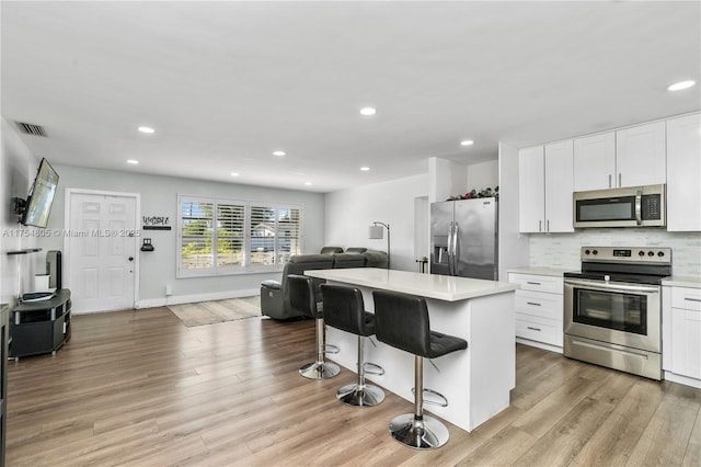 kitchen with visible vents, light wood-style flooring, a breakfast bar area, open floor plan, and stainless steel appliances