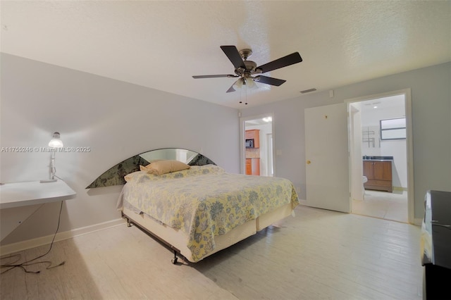 bedroom featuring light wood-type flooring, baseboards, a textured ceiling, and ensuite bath