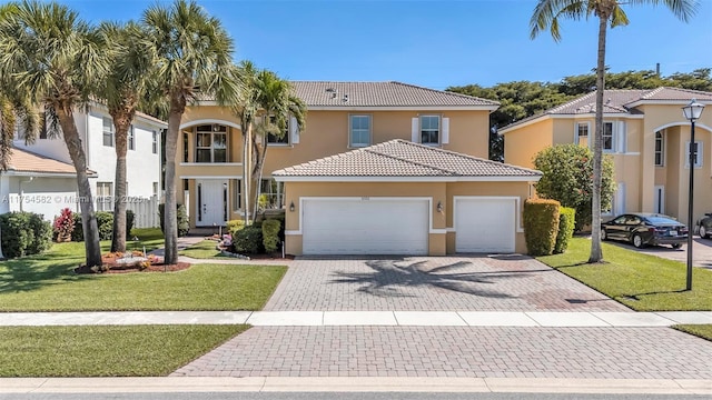 mediterranean / spanish house featuring an attached garage, a tile roof, a front yard, and stucco siding