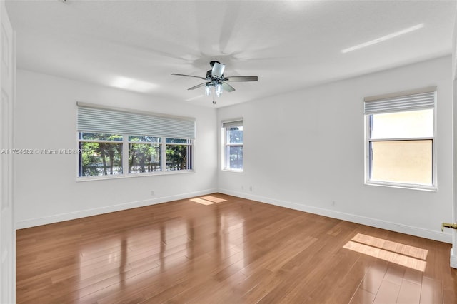 empty room with baseboards, ceiling fan, wood finished floors, and a healthy amount of sunlight