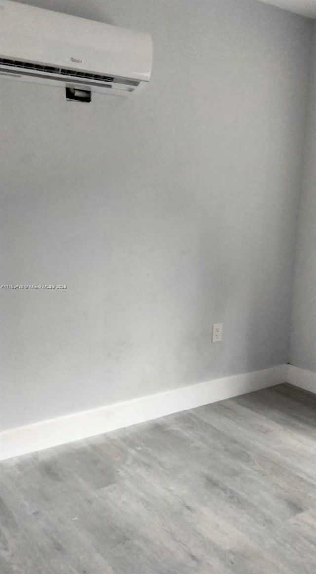 spare room with a wall unit AC, wood finished floors, and baseboards