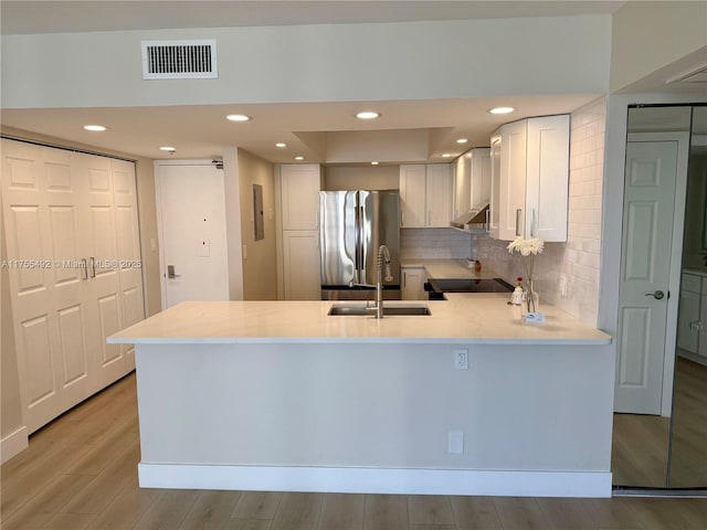 kitchen with visible vents, freestanding refrigerator, a sink, a peninsula, and under cabinet range hood