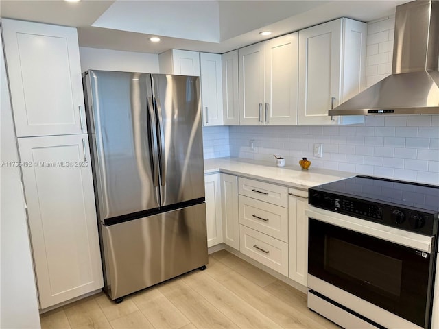 kitchen with wall chimney range hood, decorative backsplash, electric range oven, and freestanding refrigerator