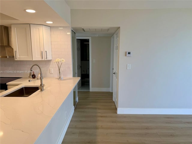 kitchen featuring decorative backsplash, light wood-style flooring, light stone countertops, wall chimney range hood, and a sink