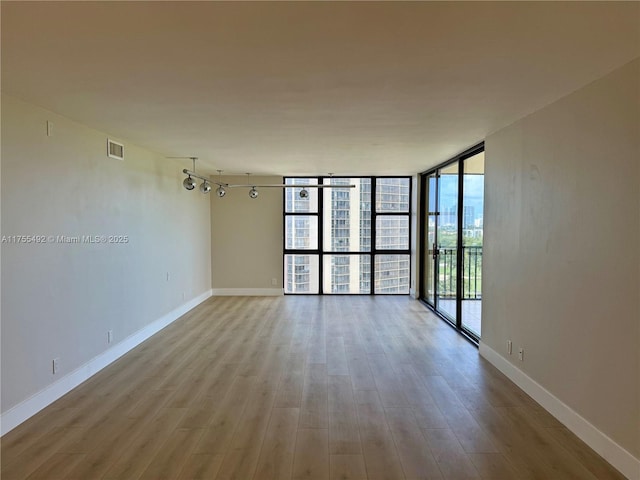 unfurnished room featuring visible vents, baseboards, wood finished floors, rail lighting, and a wall of windows