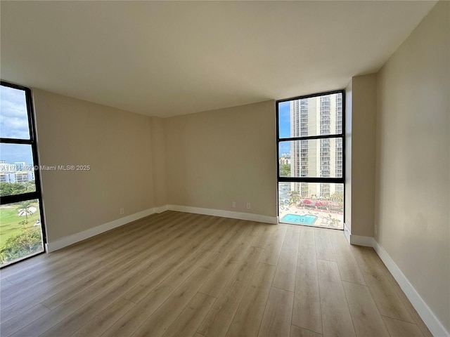 empty room with plenty of natural light, light wood-style floors, baseboards, and floor to ceiling windows