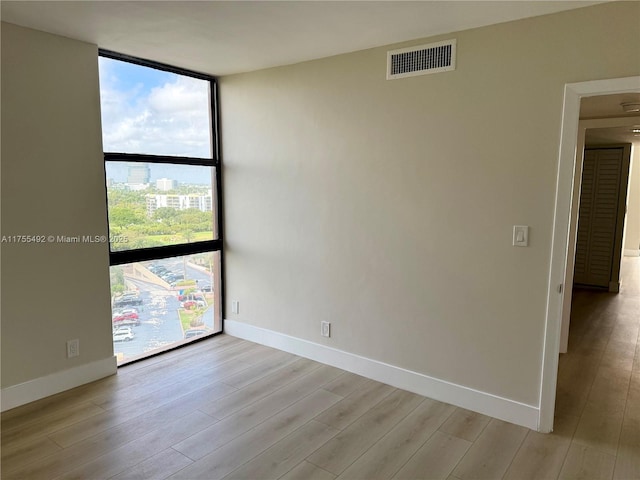 spare room featuring light wood-style floors, floor to ceiling windows, visible vents, and baseboards