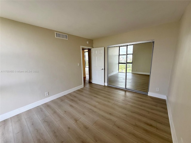 unfurnished bedroom with baseboards, a closet, visible vents, and wood finished floors