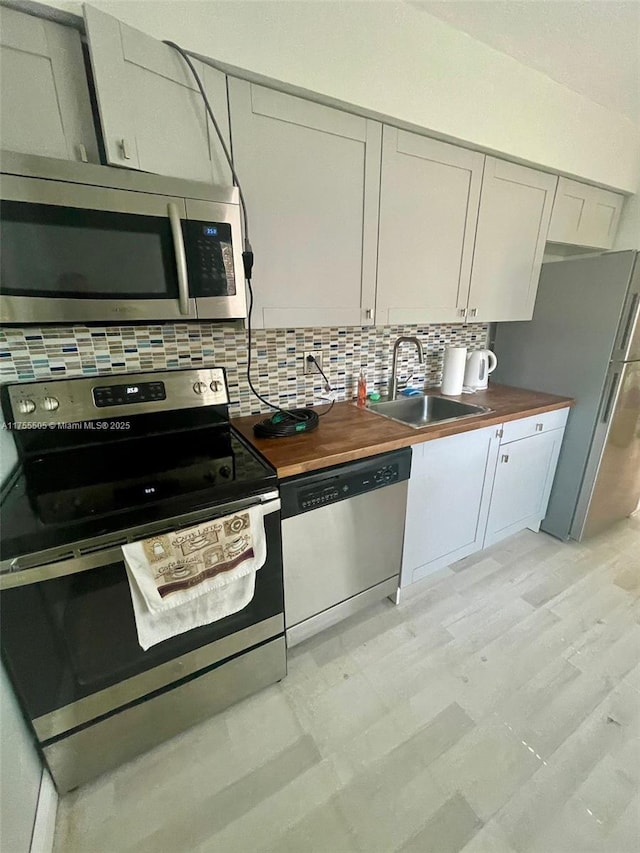 kitchen with backsplash, butcher block countertops, appliances with stainless steel finishes, and a sink