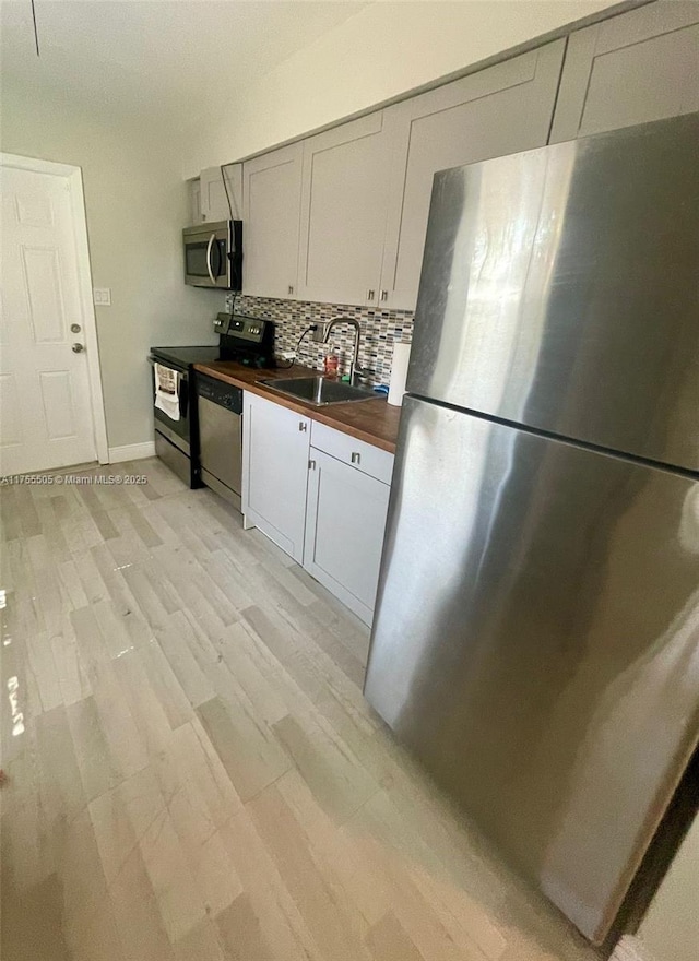 kitchen with a sink, wood counters, tasteful backsplash, stainless steel appliances, and light wood finished floors