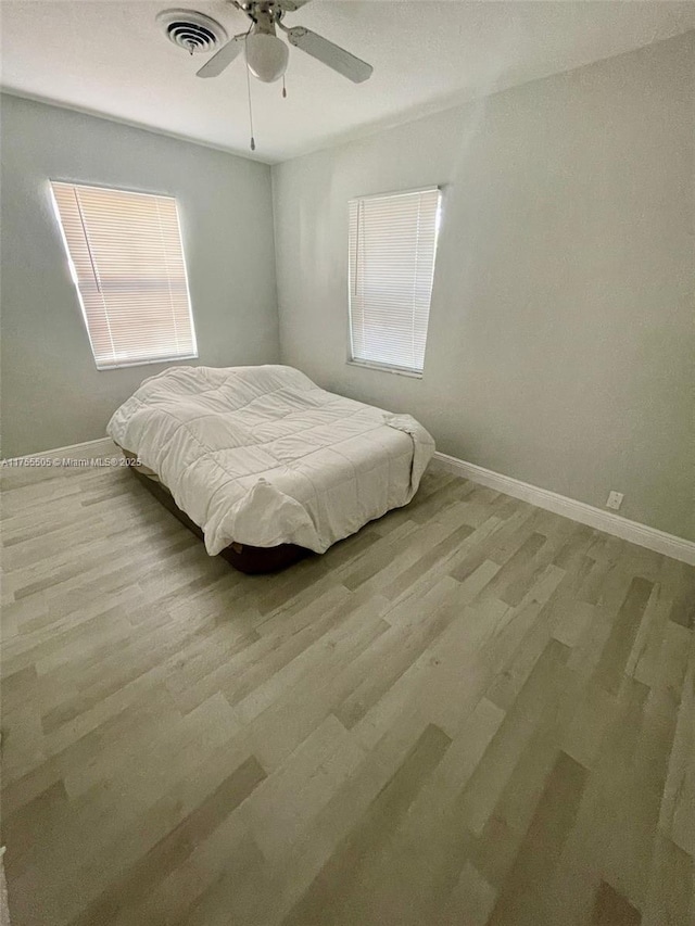 bedroom with visible vents, baseboards, wood finished floors, and a ceiling fan