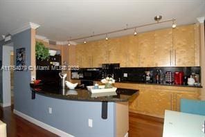 kitchen with a breakfast bar area, a peninsula, dark wood-style floors, dark countertops, and track lighting