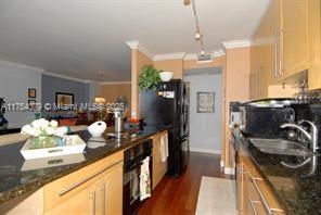 kitchen featuring dark wood finished floors, dark stone countertops, crown molding, black appliances, and a sink