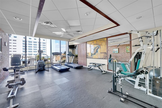 workout area with expansive windows, a drop ceiling, visible vents, and brick wall