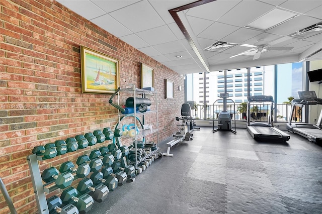 gym featuring brick wall, ceiling fan, and a drop ceiling