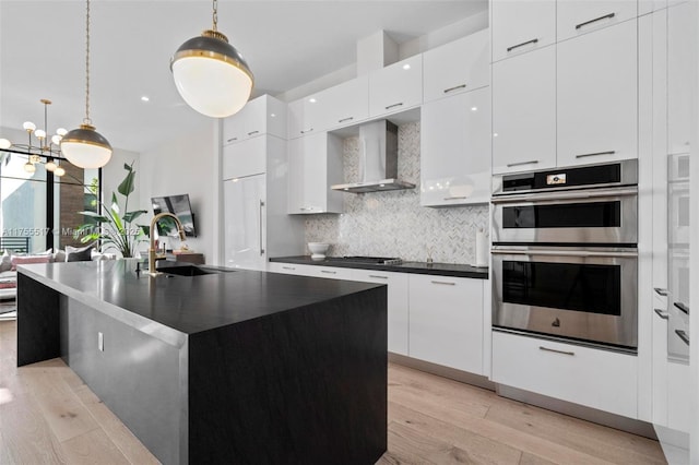 kitchen featuring dark countertops, wall chimney exhaust hood, modern cabinets, and stainless steel double oven