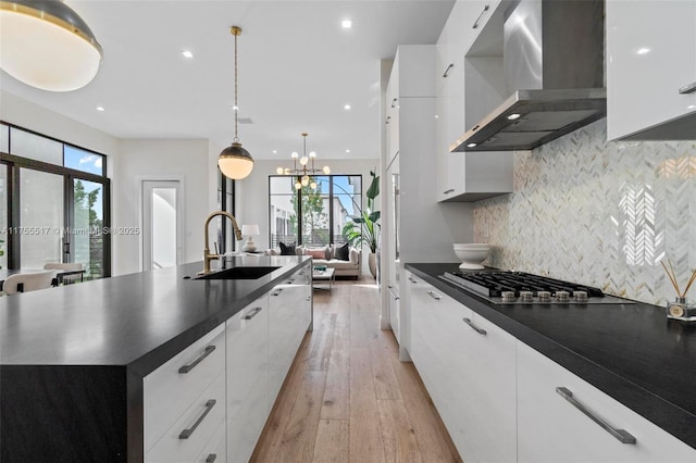 kitchen featuring a sink, stainless steel gas stovetop, dark countertops, wall chimney range hood, and modern cabinets