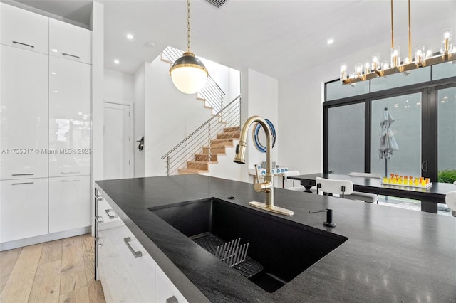 kitchen with decorative light fixtures, light wood-style flooring, modern cabinets, and a sink