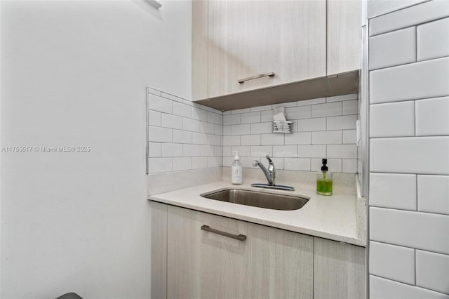 kitchen with light stone counters, light brown cabinetry, a sink, modern cabinets, and backsplash