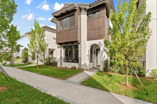 view of front of property featuring a front yard, a tiled roof, and stucco siding