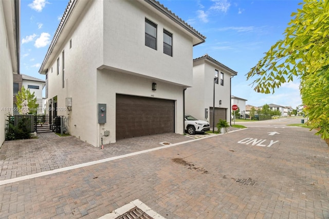 back of property featuring stucco siding, an attached garage, a tile roof, and decorative driveway