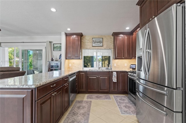 kitchen with light tile patterned floors, tasteful backsplash, appliances with stainless steel finishes, light stone counters, and a peninsula