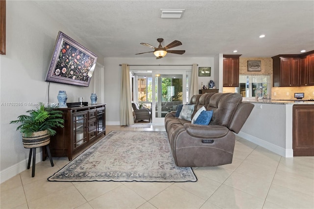 living area with light tile patterned floors, visible vents, ceiling fan, a textured ceiling, and baseboards