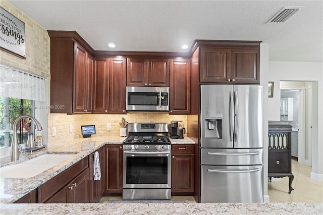 kitchen with tasteful backsplash, visible vents, appliances with stainless steel finishes, a sink, and light stone countertops