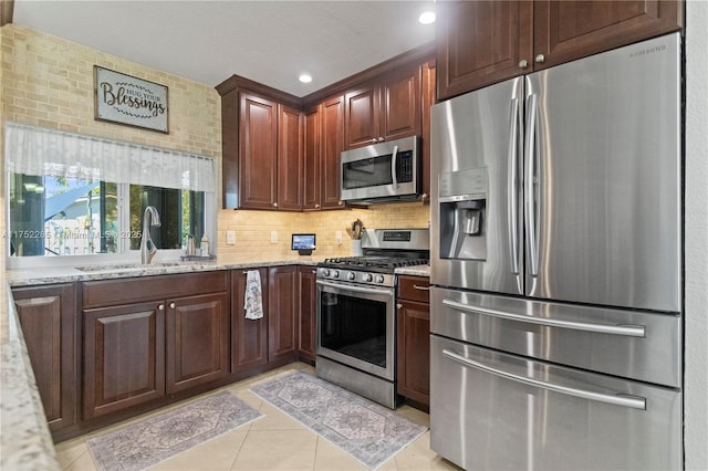 kitchen featuring light tile patterned floors, stainless steel appliances, a sink, backsplash, and light stone countertops