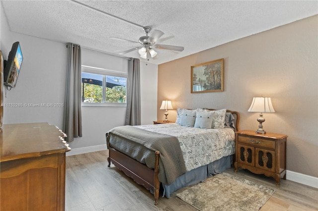 bedroom with light wood finished floors, ceiling fan, baseboards, and a textured ceiling