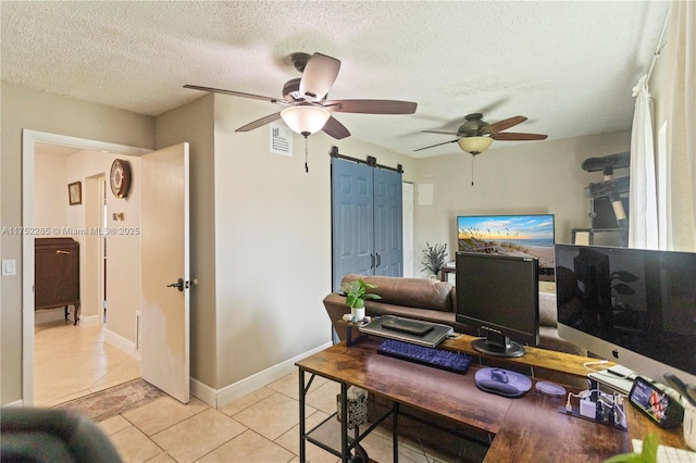 home office with light tile patterned floors, a textured ceiling, a barn door, visible vents, and a ceiling fan