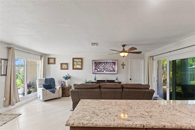 living area featuring visible vents, ceiling fan, a textured ceiling, and light tile patterned floors