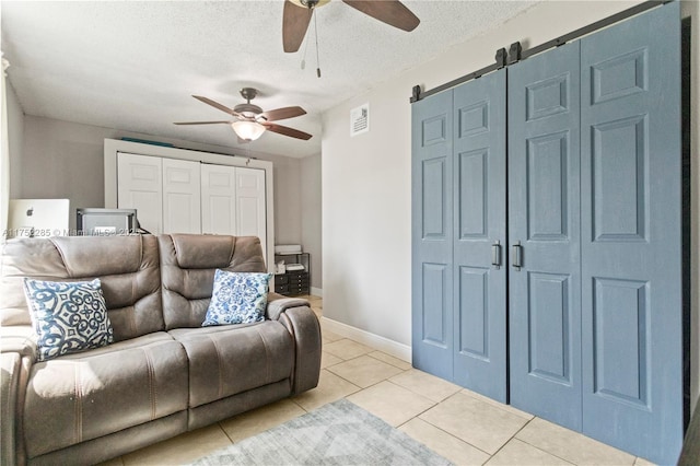 living room featuring light tile patterned floors, a textured ceiling, a barn door, visible vents, and baseboards