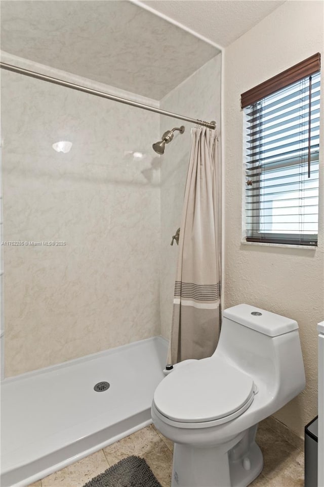 full bathroom with a textured wall, tiled shower, and toilet